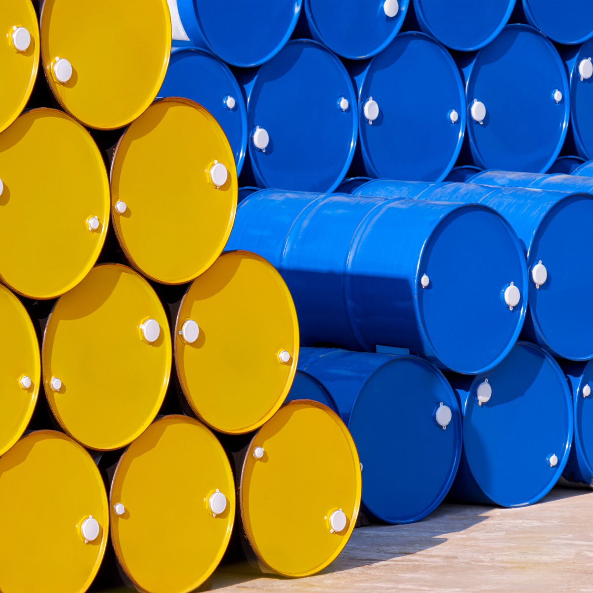 Barrels of blue and yellow chemical product stacked on a farm concrete floor